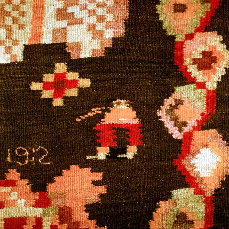 Detail of a hand-woven Moldovan carpet with red, cream and green floral and geometric motifs on a dark ground